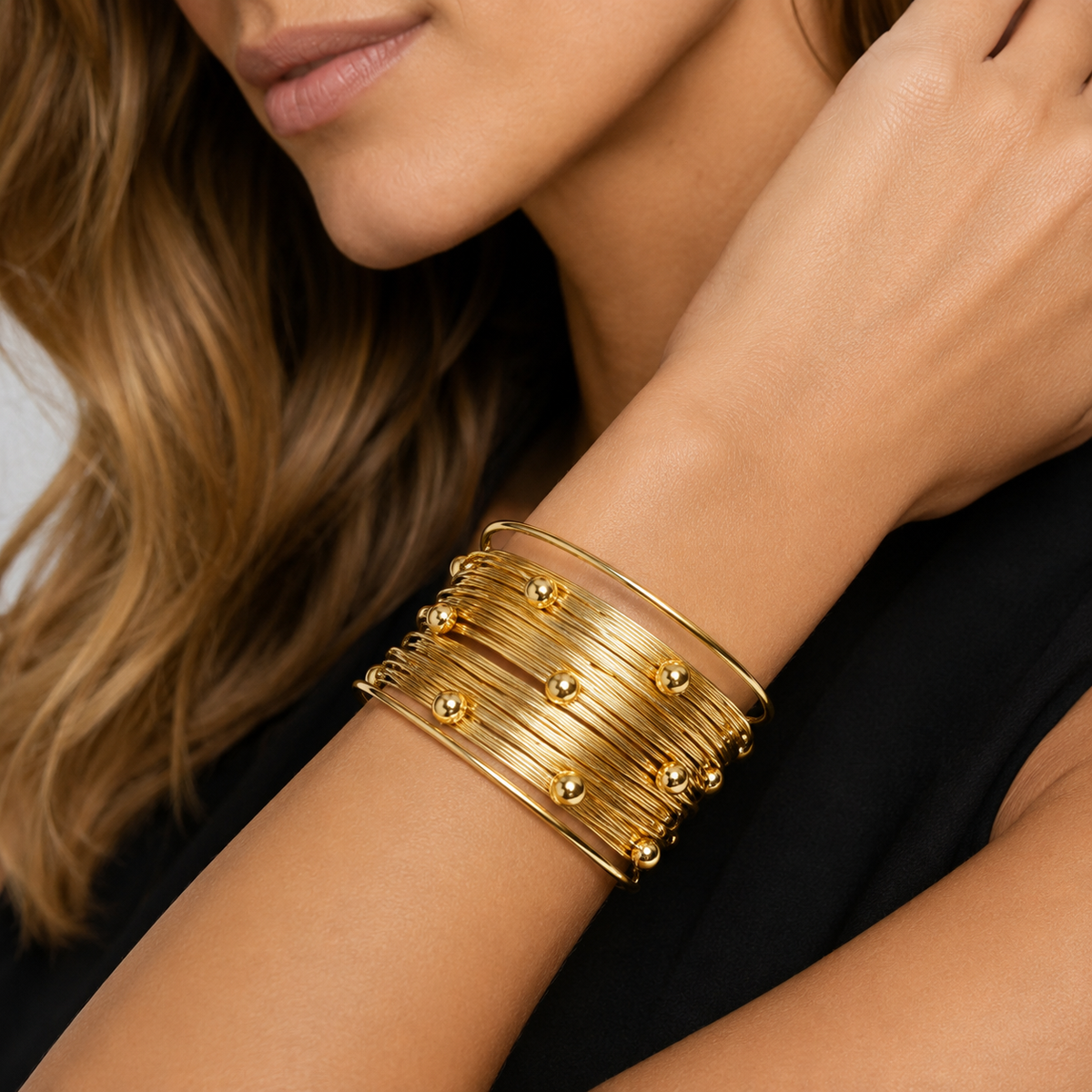 Close up detail of a layered gold wire statement cuff with delicate gold bead accents on a woman's wrist