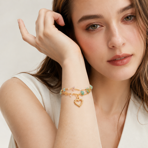 Close up of a woman wearing a delicate layered gold bracelet with pastel stones and a heart charm