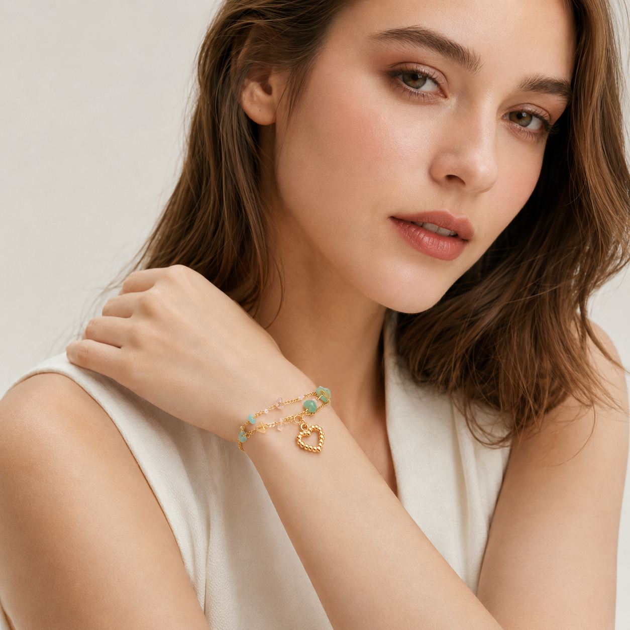 Portrait of a woman showcasing the elegant drape of a delicate gold heart and gemstone layered bracelet