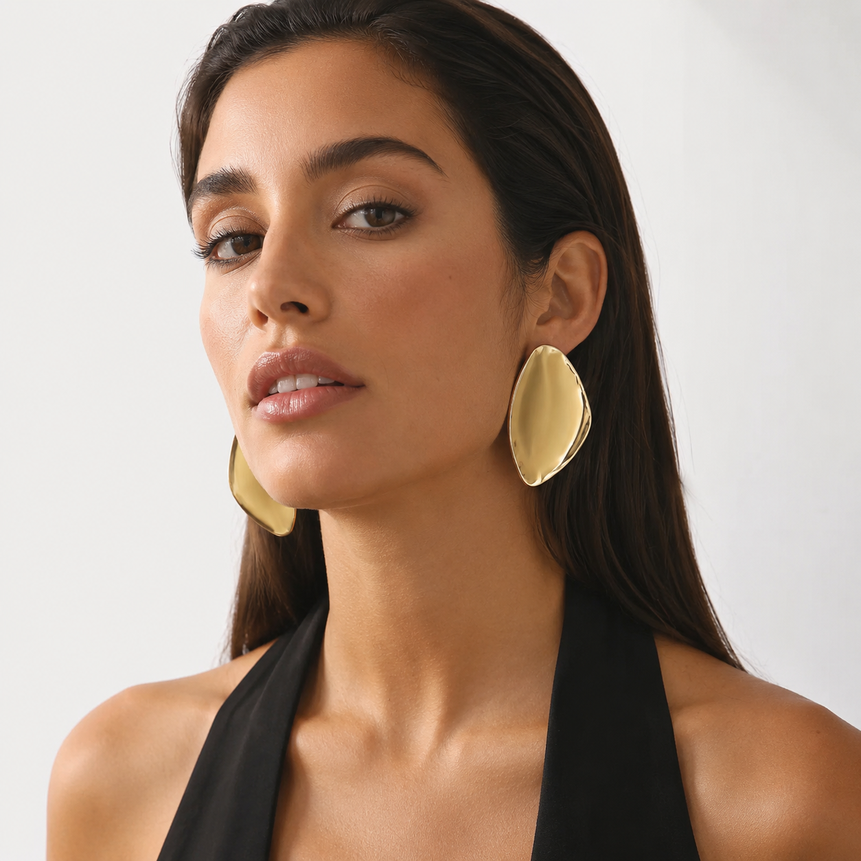 Front view of model wearing oversized liquid gold sculptural statement earrings with a black halter top