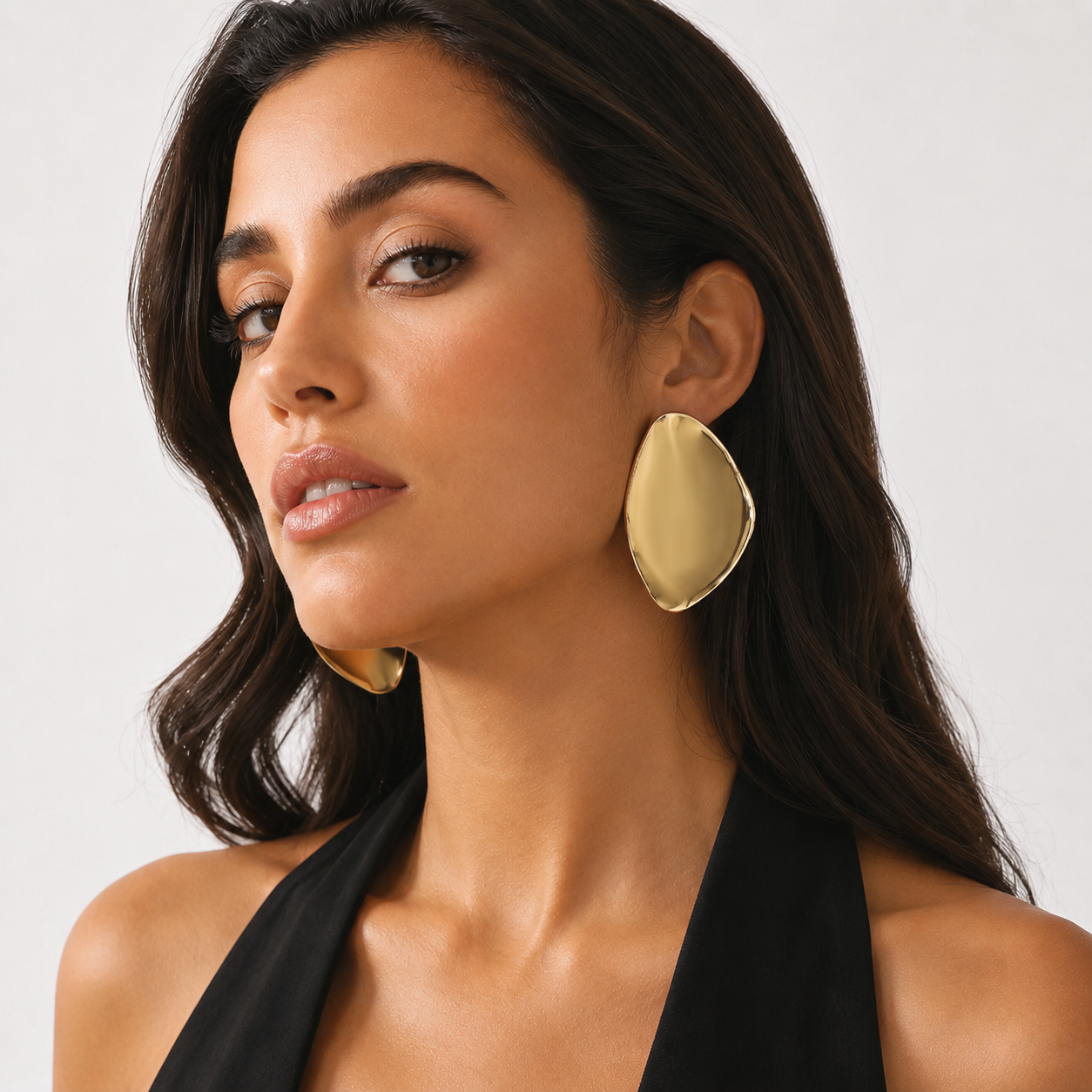 Portrait of woman with soft wavy hair wearing oversized smooth liquid metal gold studs